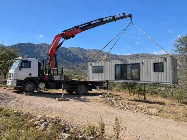 Hidrogrúa bajando una casa container en un camino de tierra de Punilla